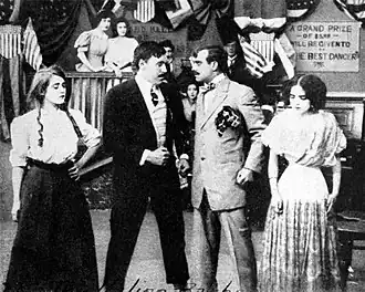 Four actors in period costume, standing close together in a dramatic scene
