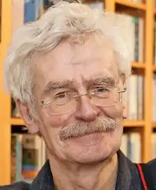 Headshot of Thomas Hertel, an elderly, white man with a moustache and tousled white hair wearing glasses.