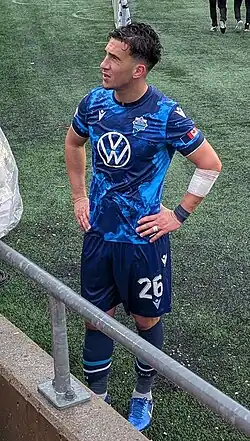 Player in a blue uniform, hands on his hips, looking left in the direction of spectators