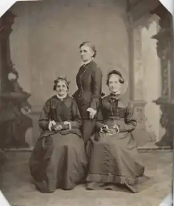 three women posing together for a portrait in 1876. the two on the left and right – Elizabeth Ann Whitney and Eliza R. Snow, respectively – are sitting, while the one in the middle – Emmeline B. Wells – stands