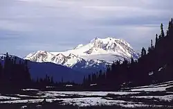 Snow-covered mountains rising over hilly vegetated terrain.