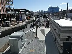 A light rail station in an urban area. A small cinderblock building is at right; a tall building is under construction at left.