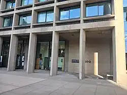Columns at the ground level of 100 Bleecker Street. The ground-story wall is twice as high as the other stories and is recessed from the facade.