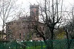 Large historic villa with turreted features behind trees.
