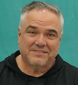 A 47-year-old man with short, gray hair, smiling at the camera with his head tilted.