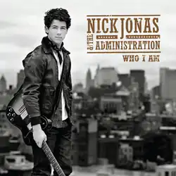 A black-and-white picture of Nick Jonas standing in front of the city skyline, holding his guitar. The band's logo and album title is showcased on the upper right corner.