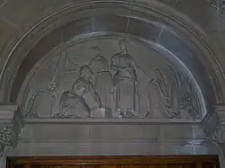Carved stone tympanum showing mill workers at the loom with a sheet of finished cloth