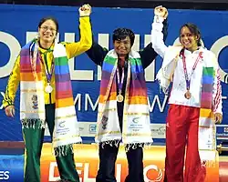 Three women wearing sporting medals raising their hands.